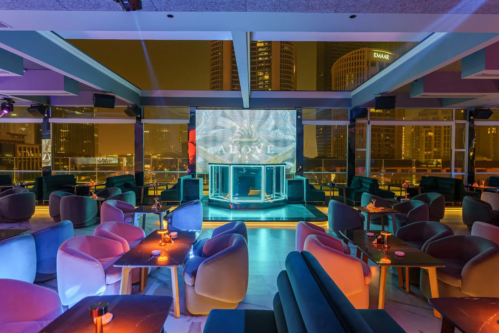 Main lounge room with glowing DJ booth and table seating at Above Rooftop Lounge